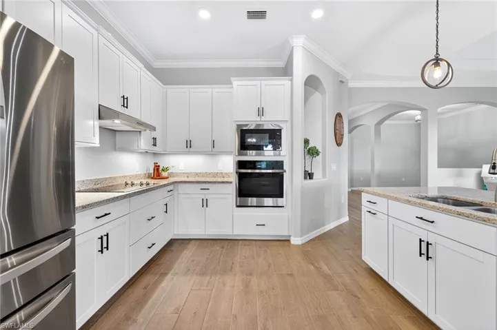 Kitchen with white cabinetry, crown molding, stainless steel appliances, pendant lighting, and light wood-style floors