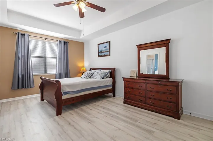 Bedroom with a raised ceiling, ceiling fan, and light hardwood / wood-style flooring