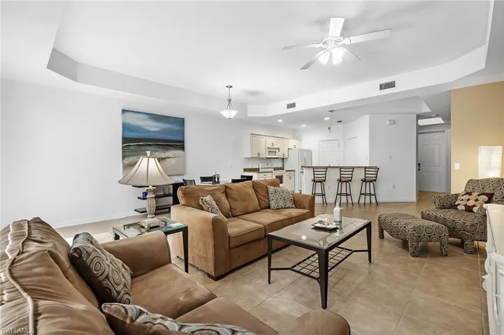 Living room with light tile patterned floors, a tray ceiling, and ceiling fan