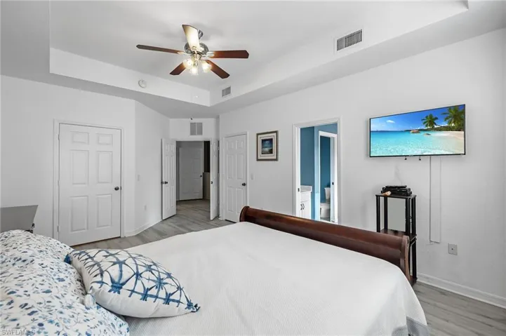 Bedroom with connected bathroom, a tray ceiling, light hardwood / wood-style flooring, and ceiling fan