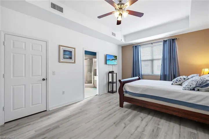 Bedroom with ceiling fan, light wood-type flooring, connected bathroom, and a tray ceiling