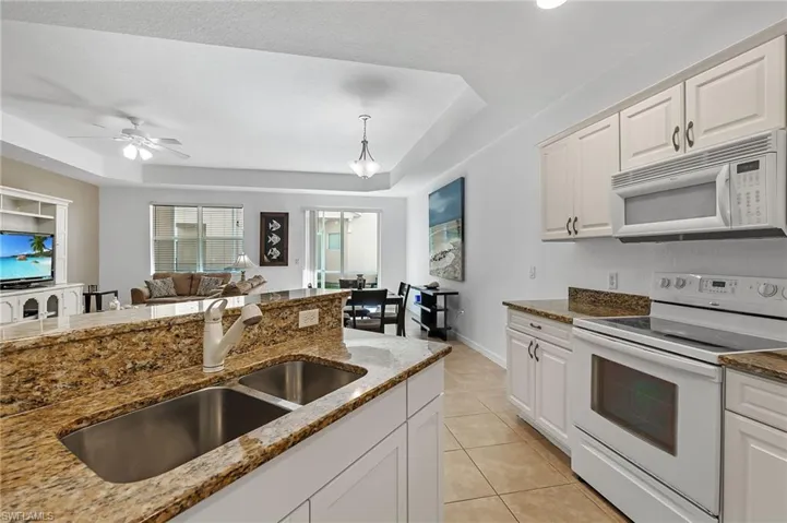 Kitchen featuring white appliances, white cabinets, sink, a tray ceiling, and stone countertops