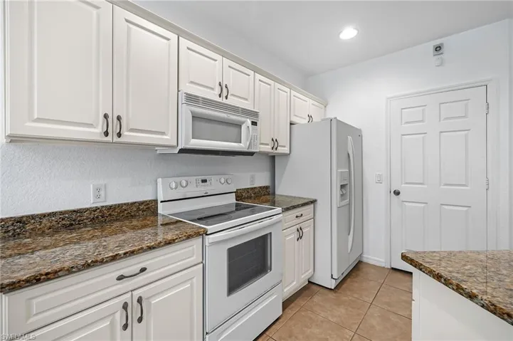 Kitchen featuring white cabinets, dark stone countertops, and white appliances