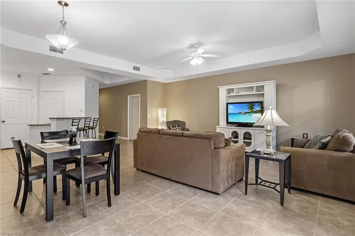Living room with a tray ceiling, ceiling fan, and light tile patterned floors
