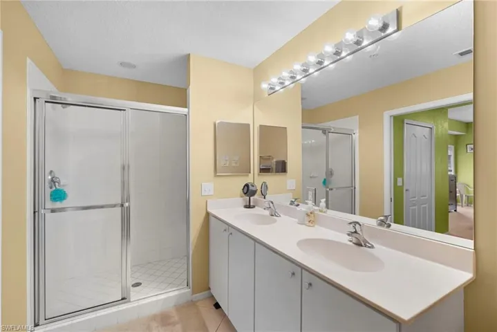 Full bath featuring double vanity, a shower stall, light tile patterned flooring, and a textured ceiling