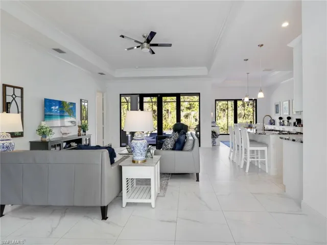 Living Room With Tray Ceiling & Ceiling Fan, Kitchen With White Shaker Cabinetry, Island , Stainless-Steel Appliances, Quartz Counters, & Pool & Wooded Rear Yard View