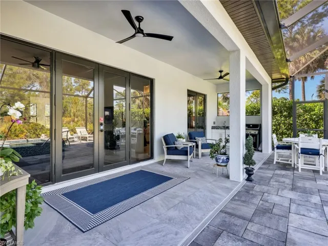 Glass Doors Leading To The Tiled Undercover Lanai With Built-In Wet Bar With Quartz Counter and Stainless Steel Sink, and Pavered Screened-In Lanai Pool Area