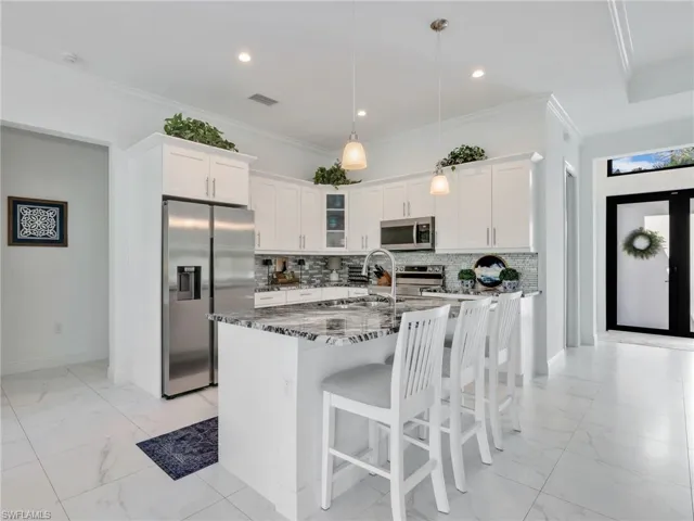 Kitchen With White Shaker Cabinetry, Island, Glass Tile Backsplash, Stainless-Steel Appliances, & Quartz Counters