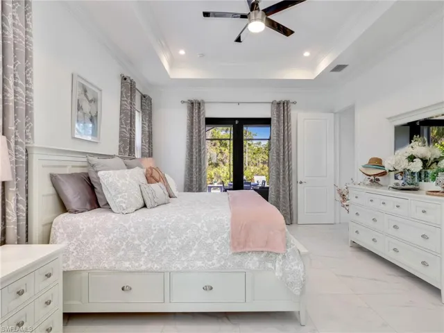 Primary Bedroom With Tray Ceiling, Ceiling Fan, & Pool & Wooded Rear Yard View