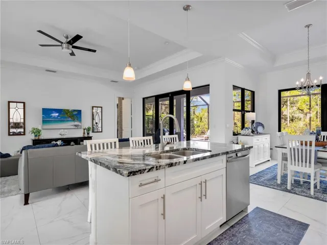 Kitchen Island With Quartz Counter and Pendant Lighting, Dining Room With Pool & Rear Wooded Yard View, & Living Room With Tray Ceiling & Pool & Rear Wooded Yard Views