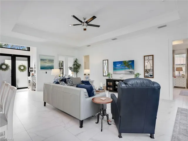 Living Room With Tray Ceiling & Ceiling Fan, Entry to Primary Bedroom, Front Entry With Double Glass Door With Transom Window, and Den
