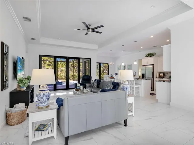 Living Room with Tray Ceiling & Ceiling Fan, Kitchen With Island, White Shaker Cabinetry, Quartz Counters, & Dining Room, & Pool & Wooded Rear Yard Views