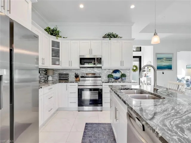 Kitchen With White Shaker Cabinetry, Island, Pendant Lighting, Glass Tile Backsplash, Stainless-Steel Appliances, and Quartz Counters