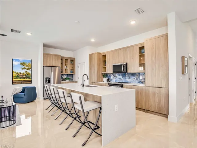 Kitchen featuring stainless steel appliances, modern cabinets, a sink, decorative backsplash, and a kitchen bar (image of model home)