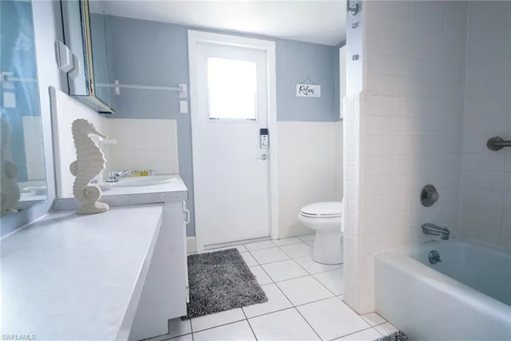 Full bath with tile walls, tile patterned floors, vanity, bathtub / shower combination, and wainscoting