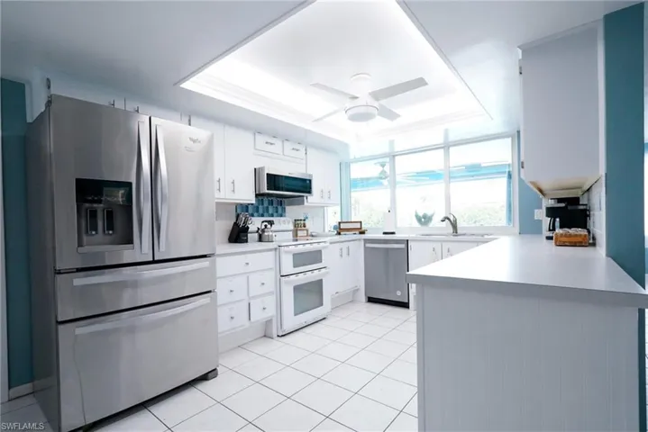 Kitchen featuring appliances with stainless steel finishes, a raised ceiling, a peninsula, backsplash, and light tile patterned flooring