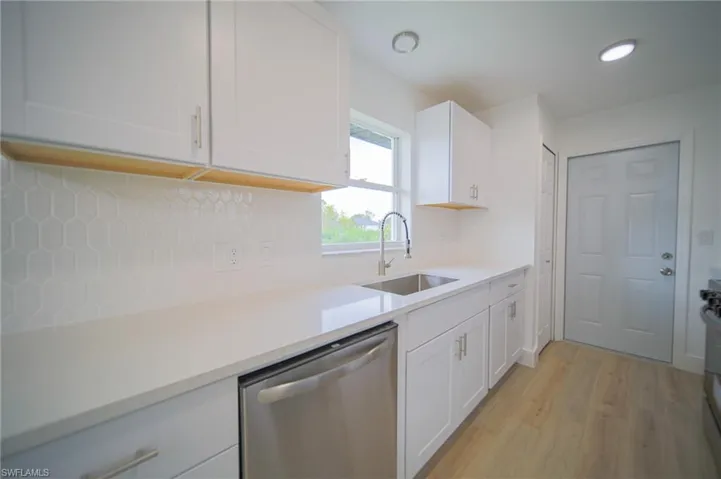 Kitchen with stainless steel dishwasher, decorative backsplash, white cabinets, light countertops, and light wood finished floors