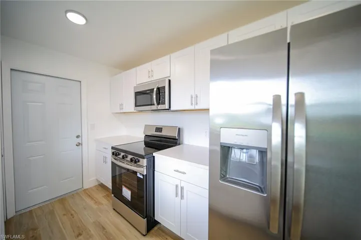 Kitchen with stainless steel appliances, light countertops, white cabinets, and light wood-style floors