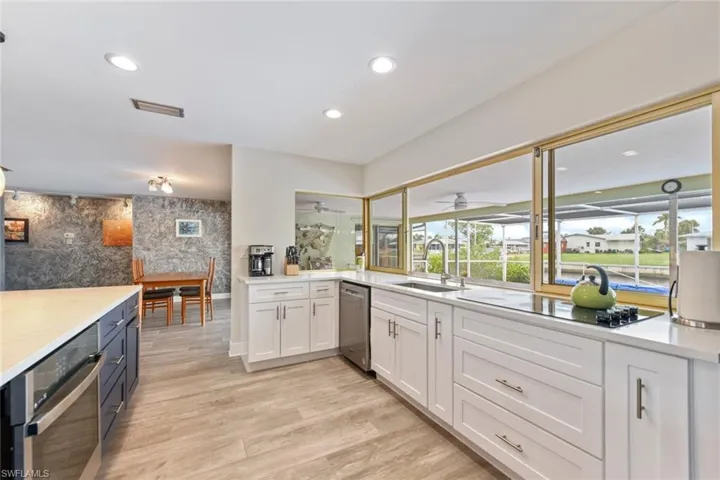 Kitchen with sink, appliances with stainless steel finishes, light hardwood / wood-style floors, light stone counters, and white cabinetry