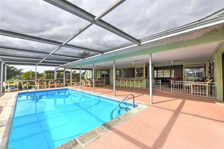 View of pool with an outdoor bar, ceiling fan, a lanai, and a patio area