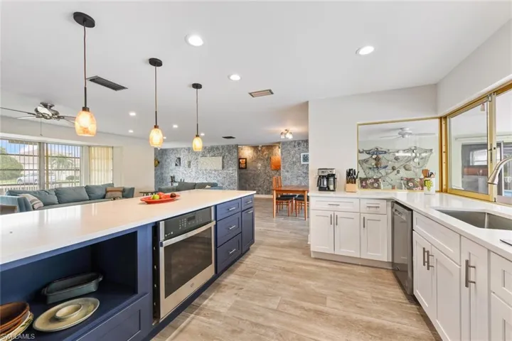 Kitchen featuring white cabinetry, sink, stainless steel appliances, pendant lighting, and light wood-type flooring