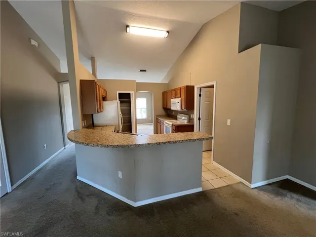 Kitchen with kitchen peninsula, vaulted ceiling, a textured ceiling, white appliances, and light carpet