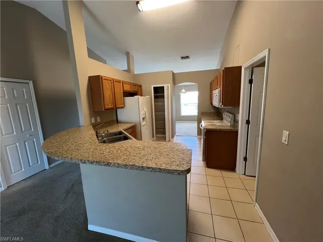 Kitchen featuring kitchen peninsula, white appliances, lofted ceiling, and sink