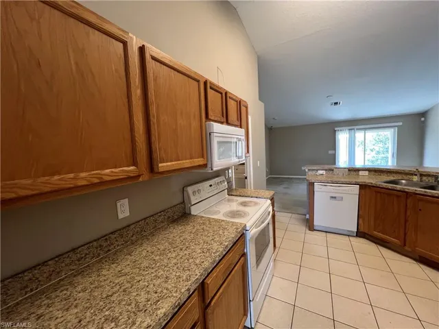 Kitchen featuring white appliances, sink, vaulted ceiling, light stone countertops, and light tile patterned floors