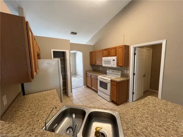 Kitchen with sink, light tile patterned floors, white appliances, and high vaulted ceiling