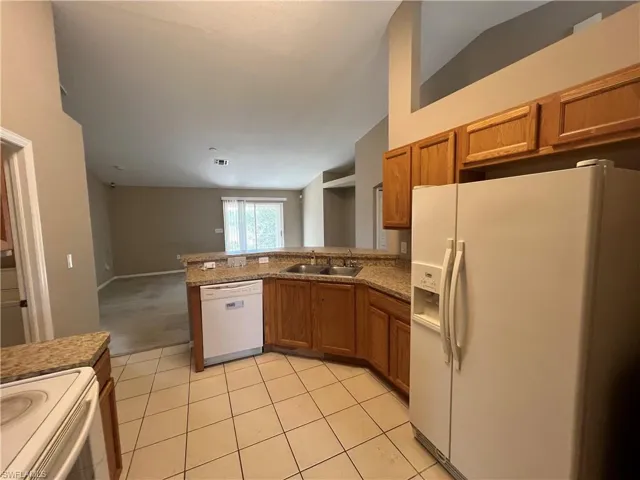 Kitchen with kitchen peninsula, white appliances, lofted ceiling, and sink