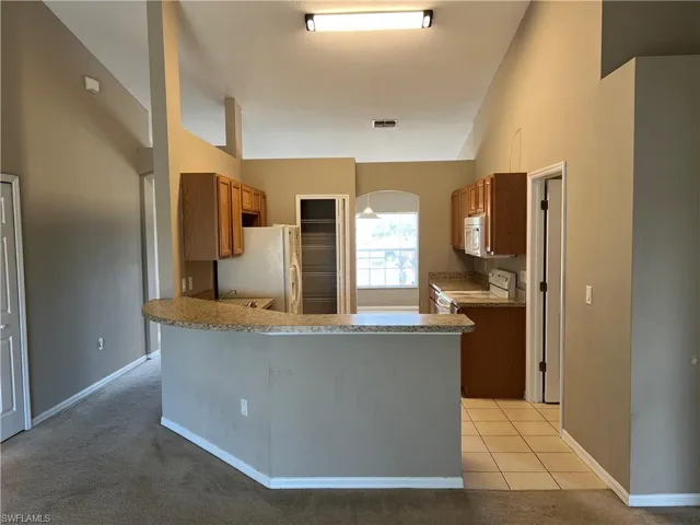 Kitchen featuring lofted ceiling, kitchen peninsula, light carpet, and white appliances