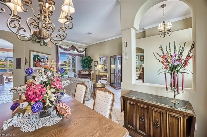 Tiled dining space with arched walkways, a chandelier, and ornamental molding