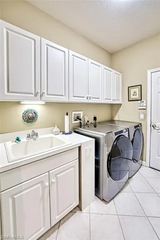 Washroom featuring light tile patterned flooring, a textured ceiling, cabinet space, and washer and dryer