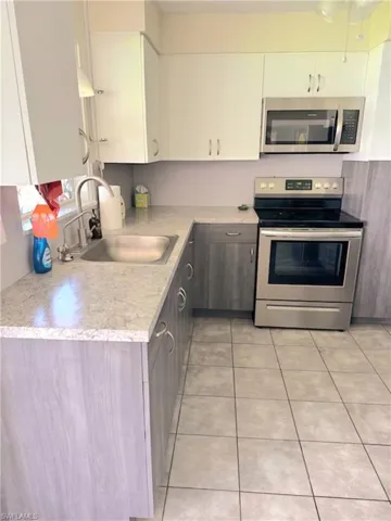 Kitchen featuring stainless steel appliances, white cabinets, sink, light stone countertops, and light tile patterned floors