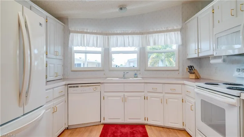 Kitchen featuring white cabinetry, white sink, white appliances, and light laminate flooring.