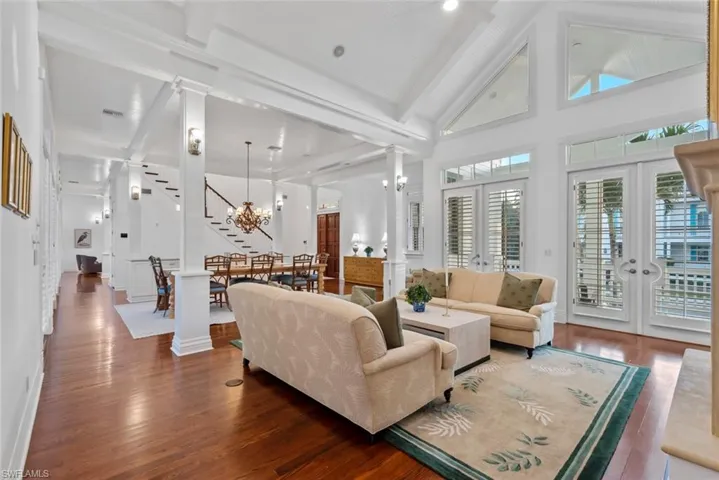 Living room with beam ceiling, decorative columns, wood floors, and stairway