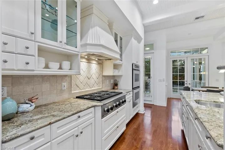 Kitchen with tasteful backsplash, dark wood finished floors, custom exhaust hood, stainless steel appliances, and cabinetry