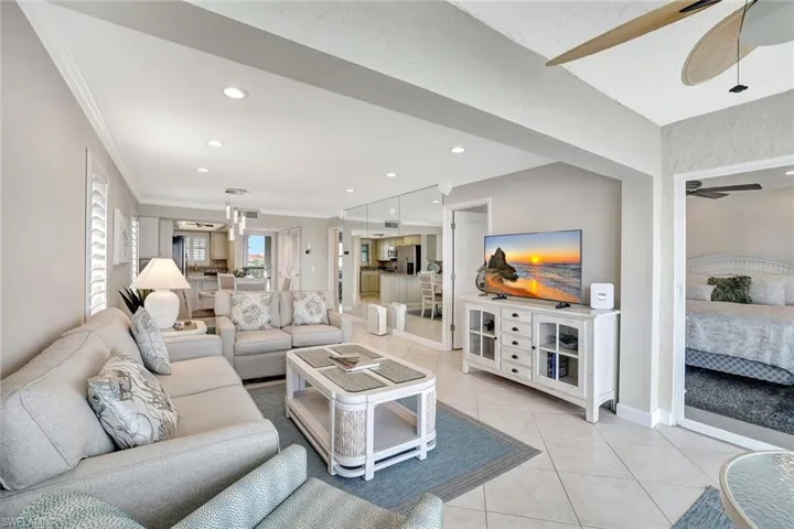 Living room featuring ceiling fan with notable chandelier, light tile patterned flooring, and crown molding