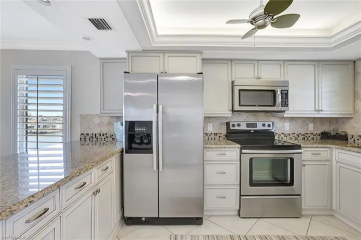 Kitchen with light stone counters, a raised ceiling, light tile patterned floors, crown molding, and appliances with stainless steel finishes