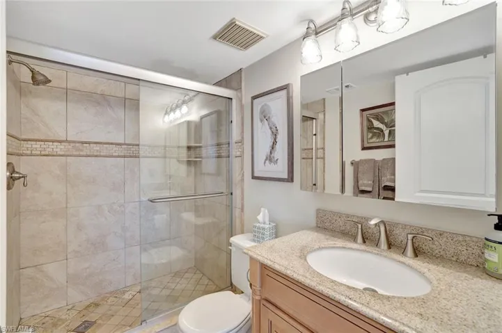 Bathroom featuring a shower with door, vanity, and toilet