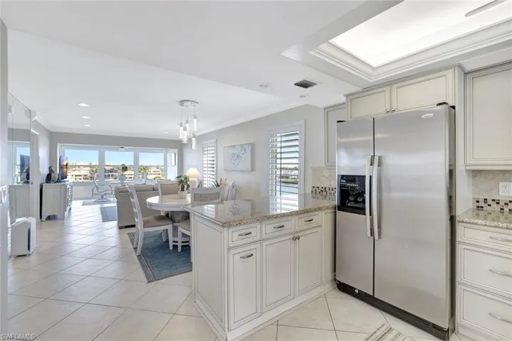Kitchen with kitchen peninsula, light tile patterned floors, tasteful backsplash, stainless steel refrigerator with ice dispenser, and crown molding