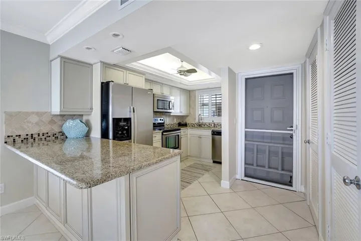 Kitchen with appliances with stainless steel finishes, light tile patterned flooring, backsplash, and light stone countertops