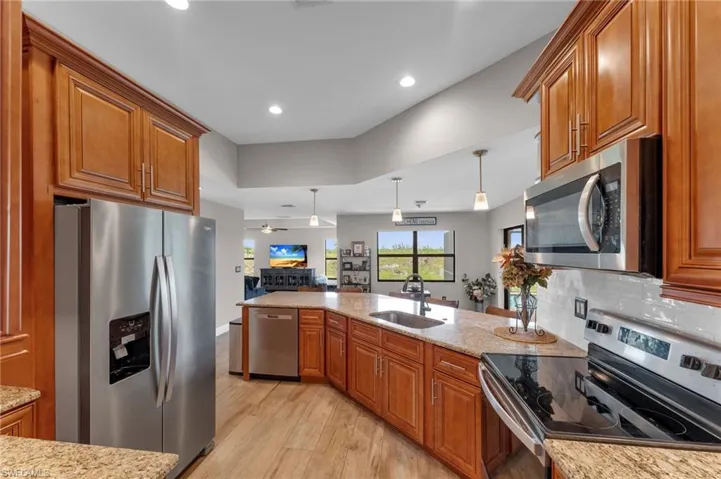 Kitchen featuring wood finish cabinets, stainless steel appliances, light stone counters, decorative light fixtures, and light wood finished floors