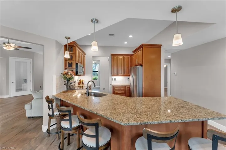 Kitchen with a kitchen breakfast bar, wood finish cabinets, decorative light fixtures, stainless steel appliances, and light stone countertops