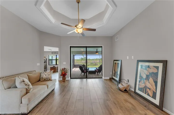 Living area with a tray ceiling, light wood finished floors, and a ceiling fan