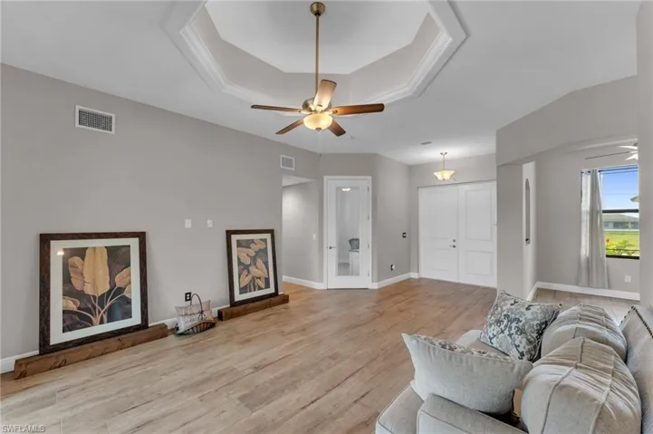 Living room with ceiling fan, a raised ceiling, and light wood-style flooring