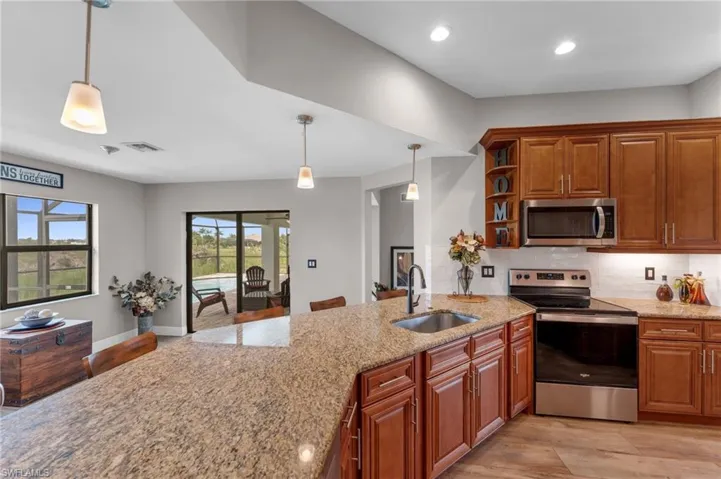 Kitchen with stainless steel appliances, wood finish cabinetry, light wood-type flooring, light stone countertops, and pendant lighting