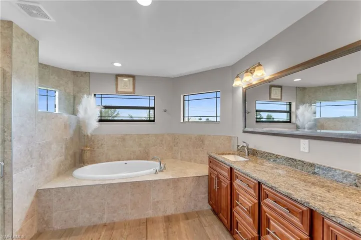 Bathroom with vanity, a bath, light wood finished floors, and a tile shower
