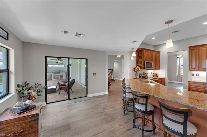 Kitchen featuring wood finish cabinetry, light stone counters, a breakfast bar area, pendant lighting, and a peninsula