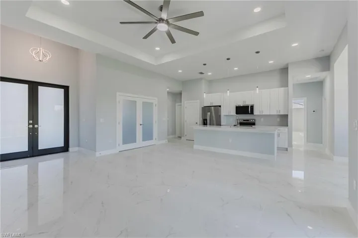 Unfurnished living room featuring french doors, a high tray ceiling, a ceiling fan, recessed lighting, and light marble finish flooring